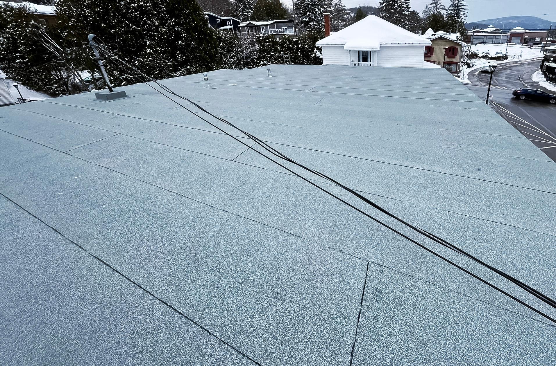 Toiture plate recouverte d’une membrane élastomère grise en hiver avec câbles électriques apparents.