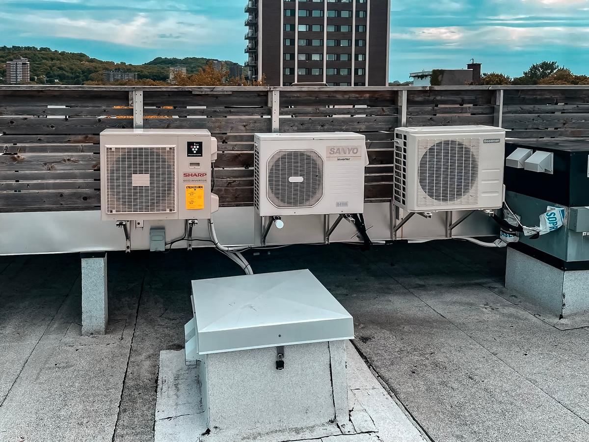 Unités de climatisation extérieures installées sur un toit plat avec vue sur des immeubles résidentiels et collines verdoyantes à l'arrière-plan.