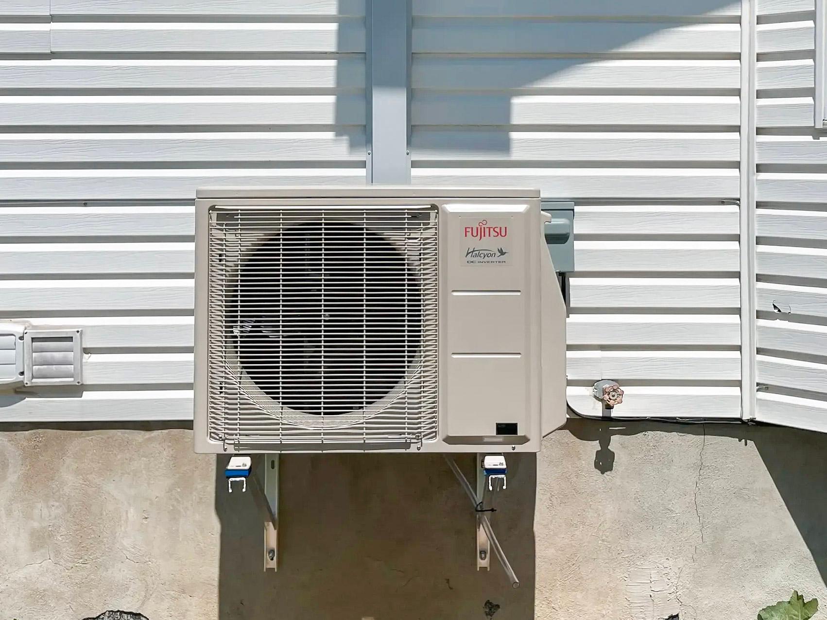Unité extérieure de thermopompe Fujitsu Halcyon installée sur un mur blanc d'une maison résidentielle, montée sur un support métallique pour un système HVAC moderne, offrant chauffage et climatisation avec une efficacité énergétique optimale, assurant le confort thermique.