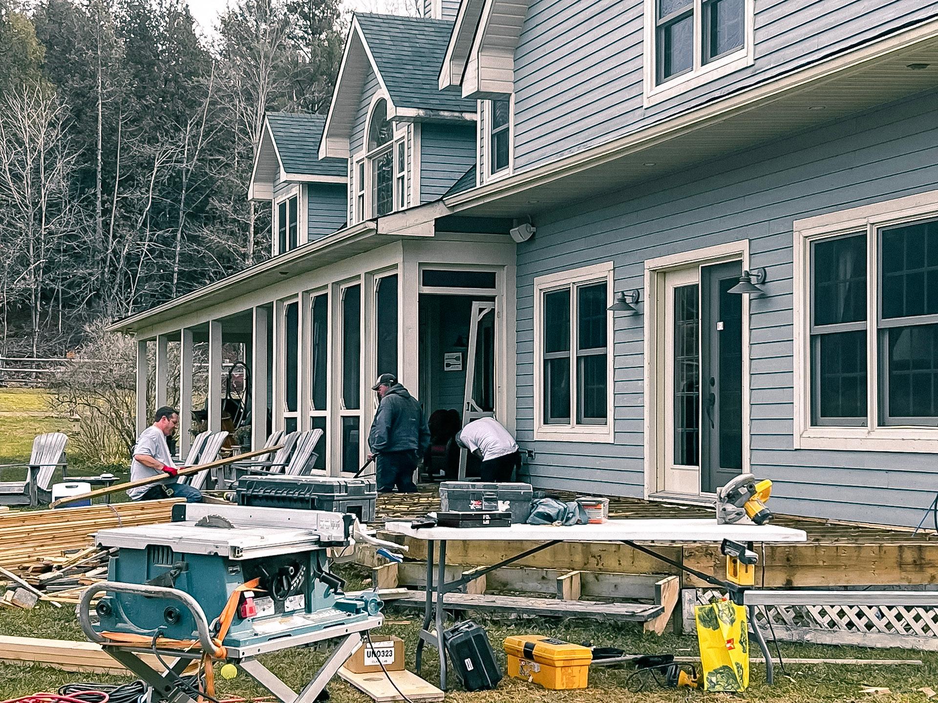 Travailleurs rénovant la terrasse en bois d'une maison bleue avec outils et équipements de construction.