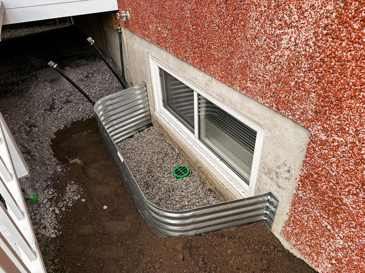 Margelle en métal installée devant une fenêtre de sous-sol avec drainage en gravier et grille de protection