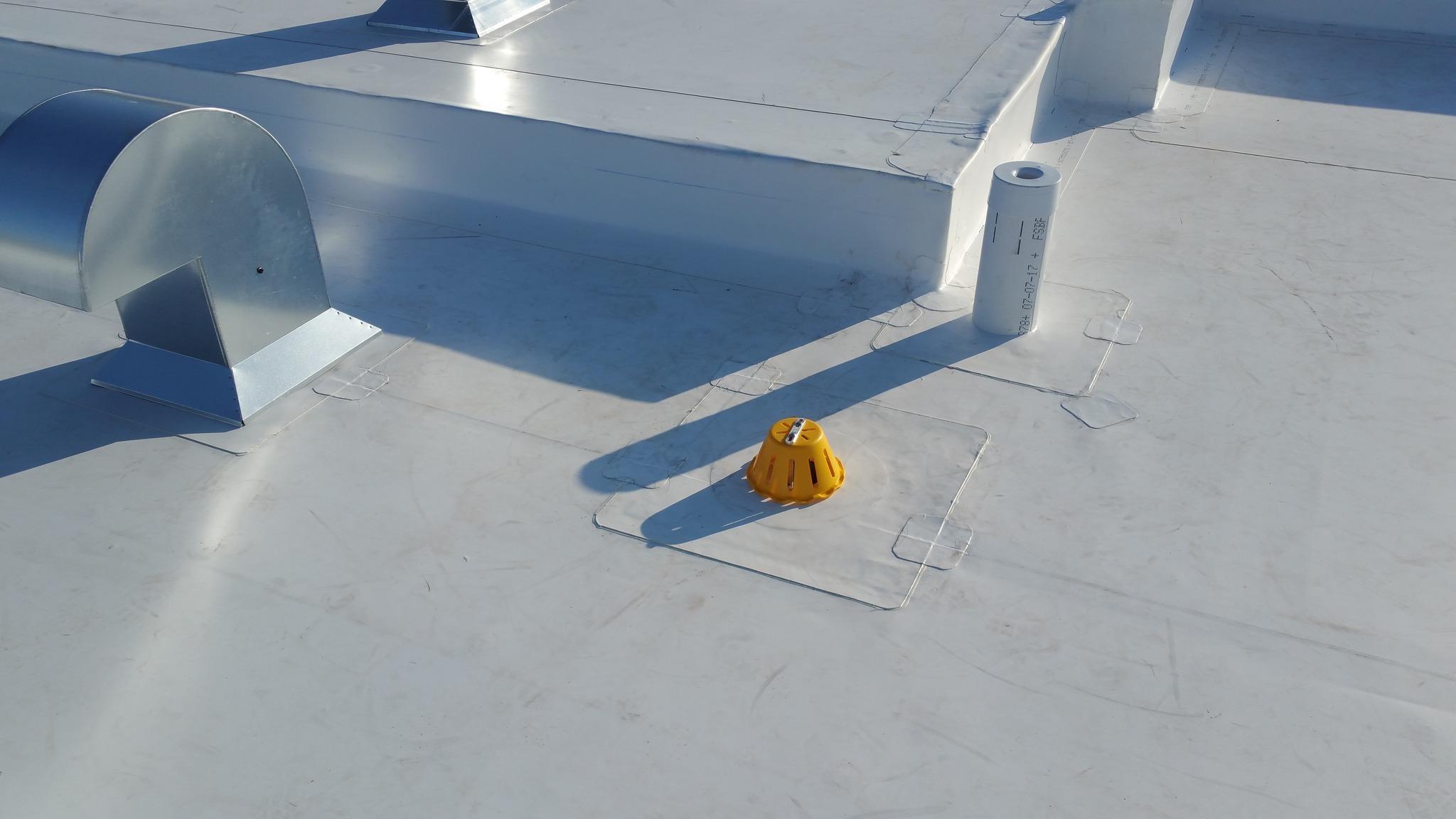 Toiture plate en membrane blancheen TPO avec sorties de ventilation, drain protégé par un couvercle jaune et détails d’étanchéité visibles.