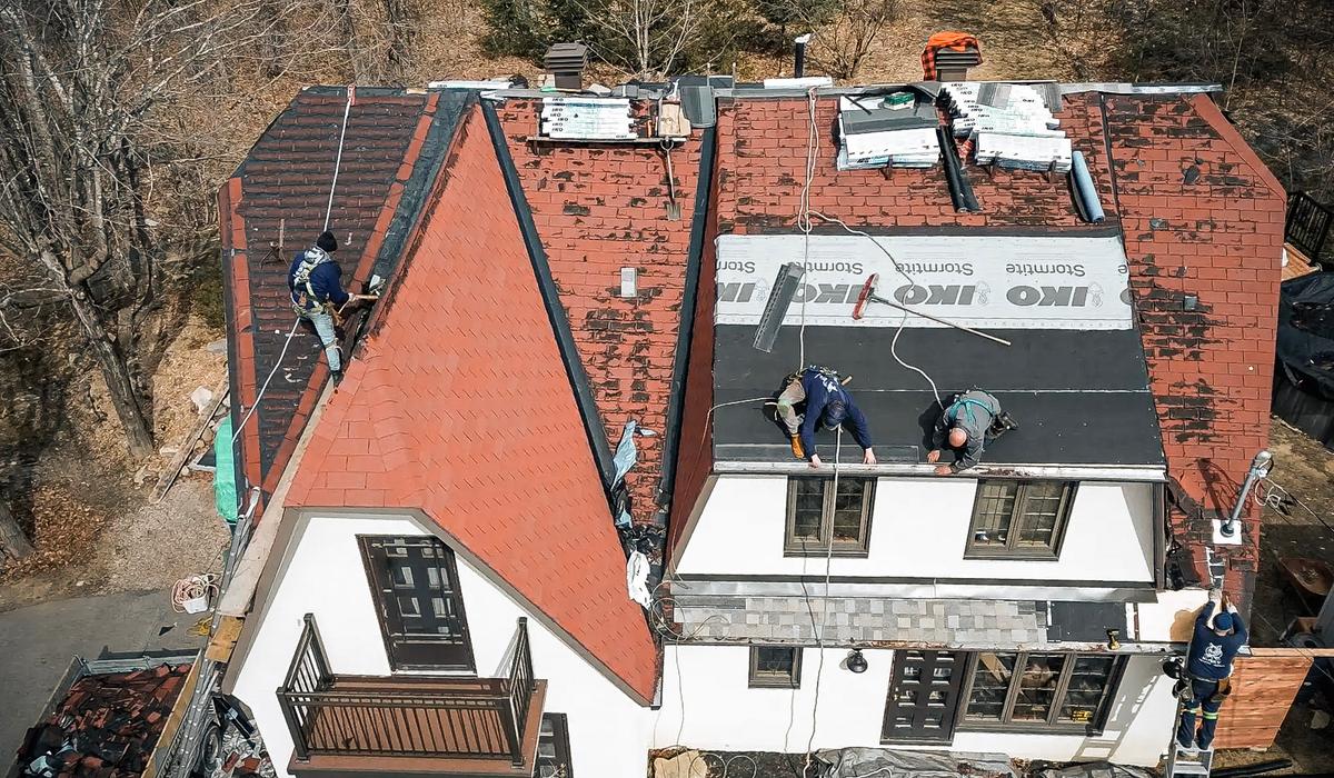 Travaux de rénovation de toiture avec pose de bardeaux rouges sur une maison à étages.