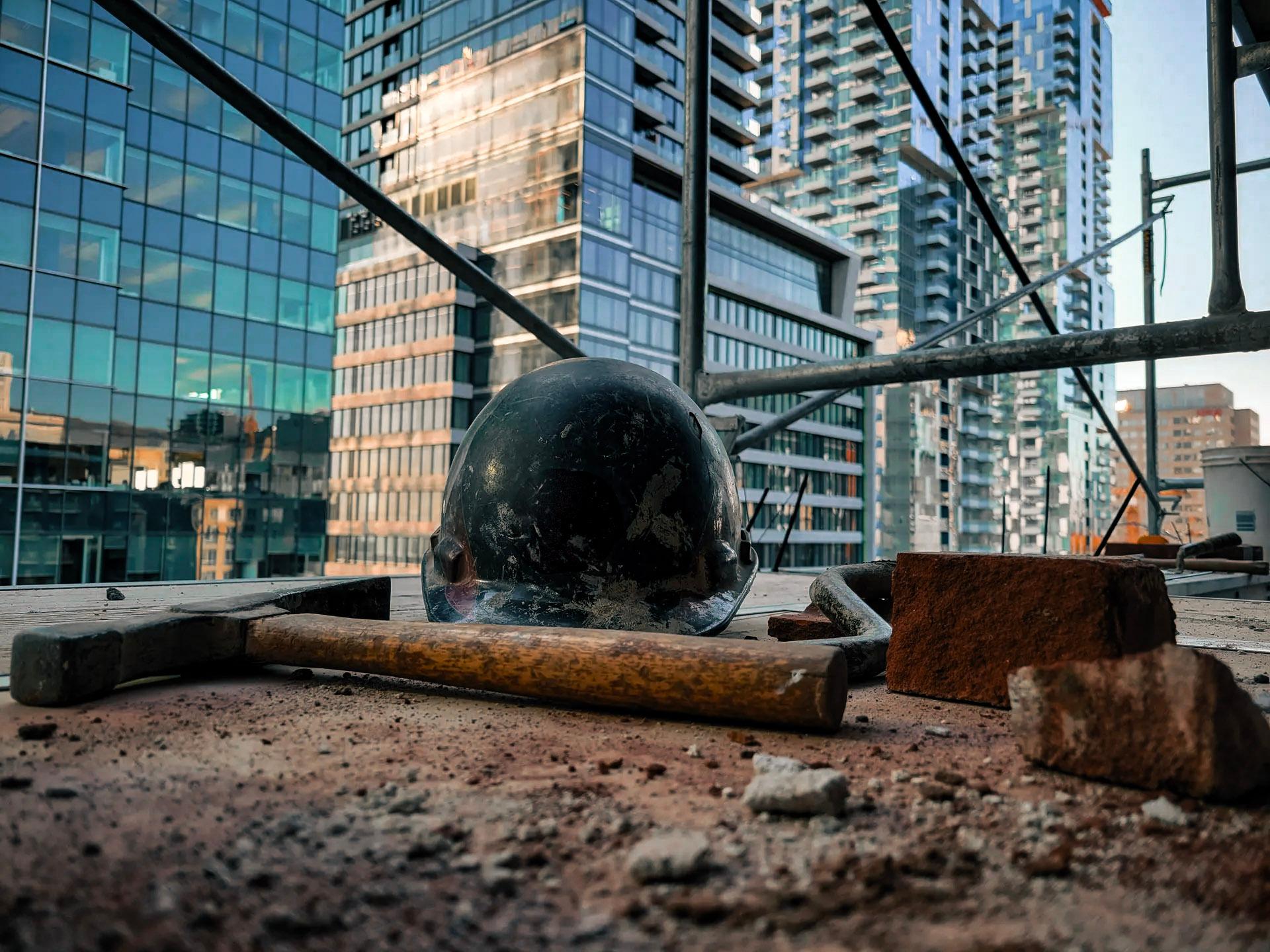 &nbsp;Vue d'un chantier en hauteur avec un casque de sécurité, un marteau et des briques, entouré d'immeubles modernes en arrière-plan.