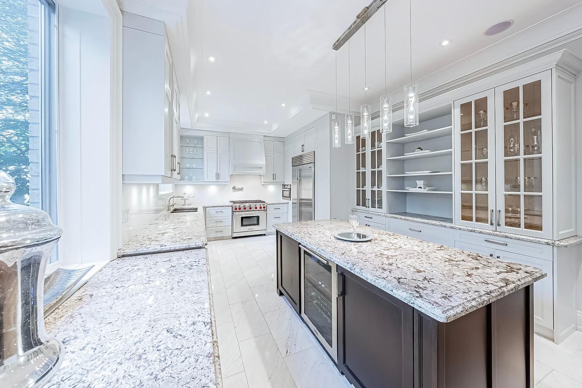 Cuisine luxueuse tout en blanc avec comptoirs en granite, îlot central avec cave à vin et éclairage suspendu.