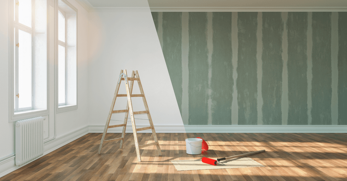 Rénovation d'une pièce : moitié du mur repeinte en vert clair, peinture blanche sur l'autre moitié, échelle en bois, pot de peinture et rouleaux, sol en parquet.